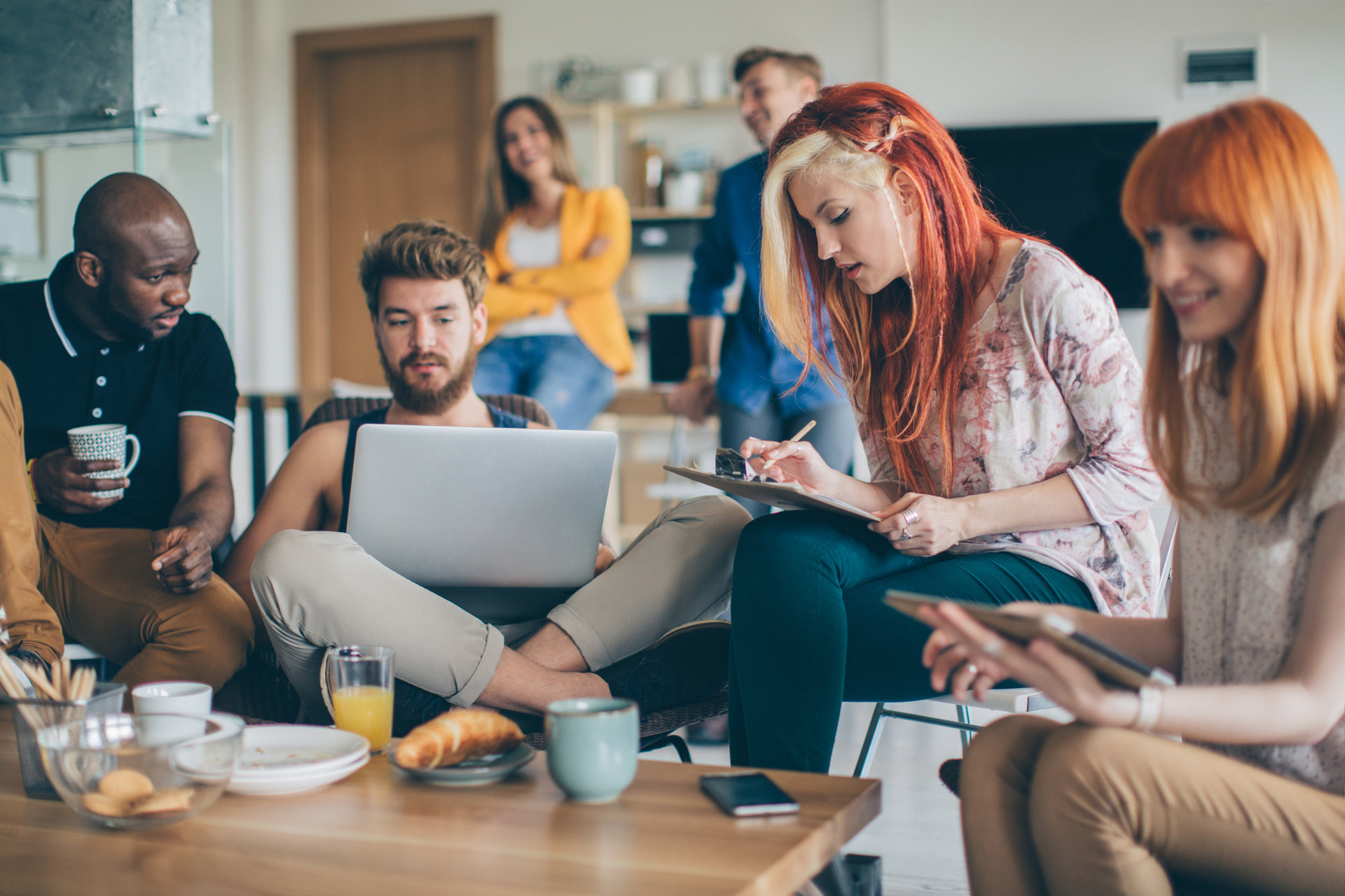 Group of young people spending their time in common living room. Checking their gadgets to catch up with latest news or messages or studying. They are friends who sharing living space.